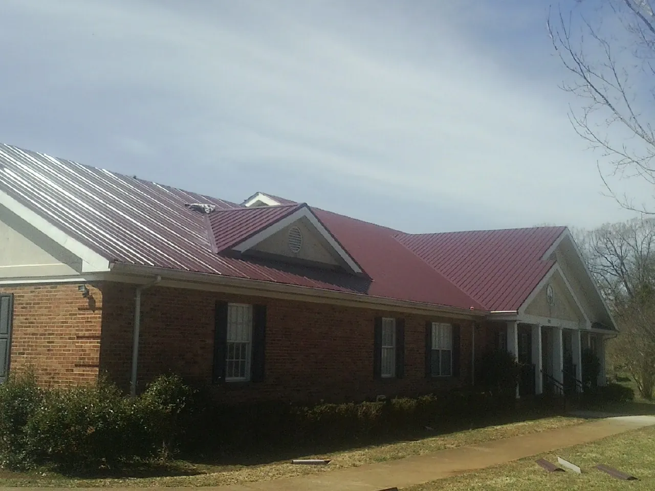 Red metal roof with gabled entries on a long brick building, from a Hail Damage Roof Repair job in Clarkdale
