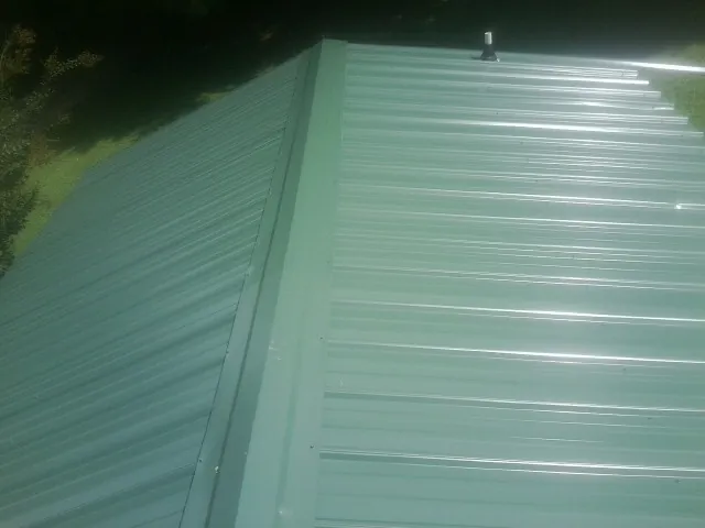 New green metal panels meeting at the ridge of a roof — Flat Roof Repair work by our crew in Clarkdale