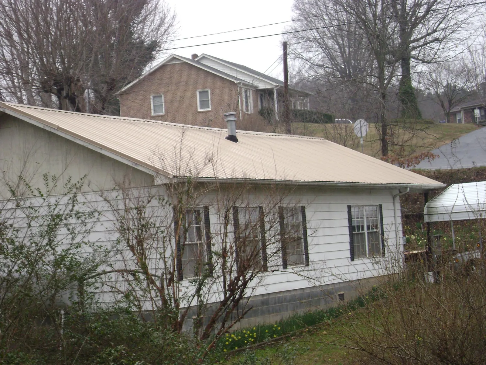 Tan metal roof on a white sided house set into a hillside — Commercial Roofing by Roofing Brothers in Clarkdale